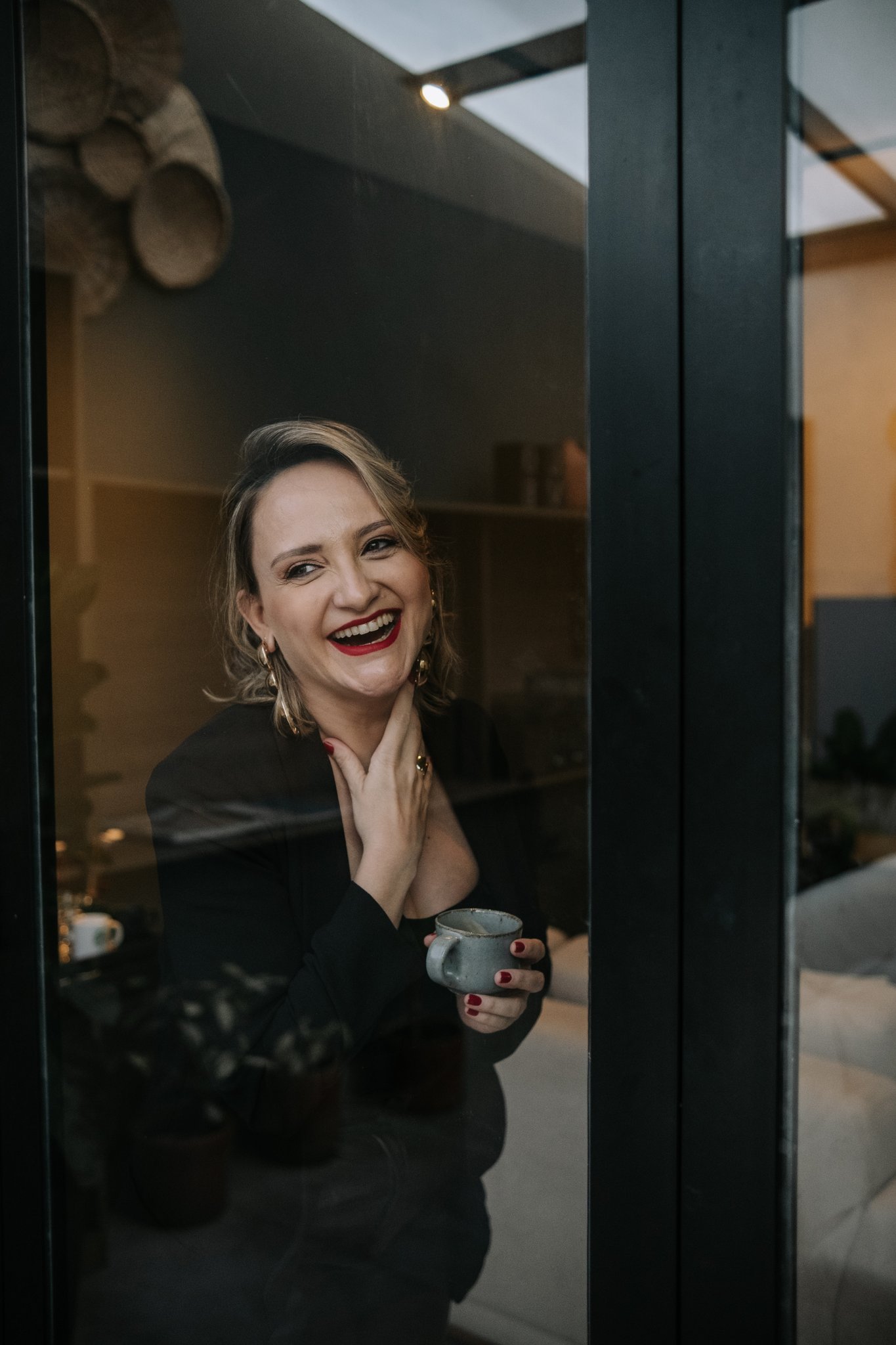 Dra. Catarine Padoveze rindo, com uma xícara de café, na porta da clínica em Santo André